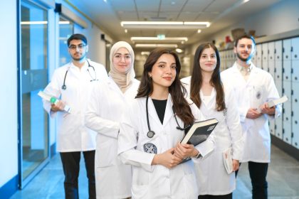 Grupo diverso de estudantes de Medicina usando jalecos em um corredor universitário.